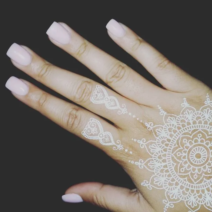 White henna-inspired tattoo on hand, resembling elegant lace patterns.