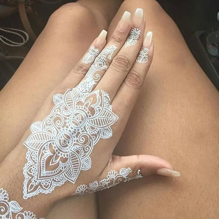 White henna-inspired tattoo on hand, resembling elegant lace with intricate floral patterns.