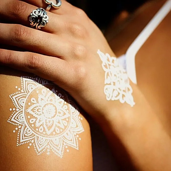 White henna-inspired tattoos on skin, resembling elegant lace patterns with intricate floral designs.