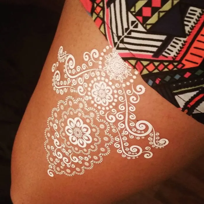 White henna tattoo resembling elegant lace on a person's thigh.