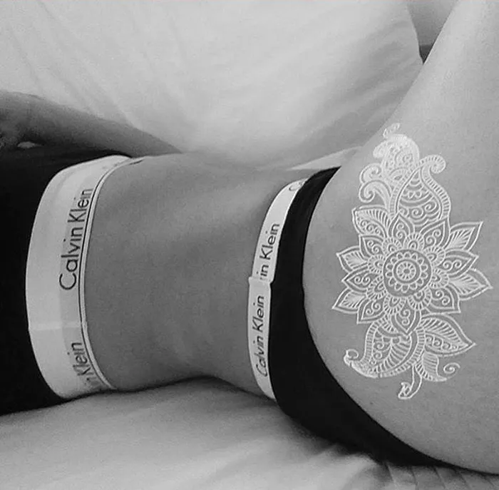 White henna-inspired tattoo on hip resembling elegant lace, in an artistic black and white setting.