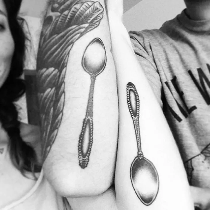 Couple's arms with matching spoon tattoos, showcasing brave wedding tattoo choice over traditional rings.