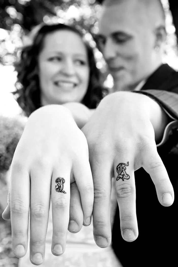 Couple displaying matching wedding tattoos on their ring fingers, opting for inked symbols instead of traditional wedding rings.