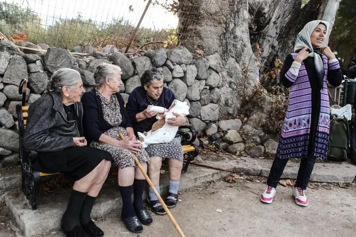 3 Old Greek Ladies In Lesvos, Feed, Sooth And Sing To Crying Refugee Baby, While Mother Smiles