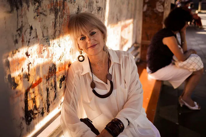 Woman in a white blouse, sitting against a graffiti wall, photographed by a Romanian photographer showcasing universal beauty.