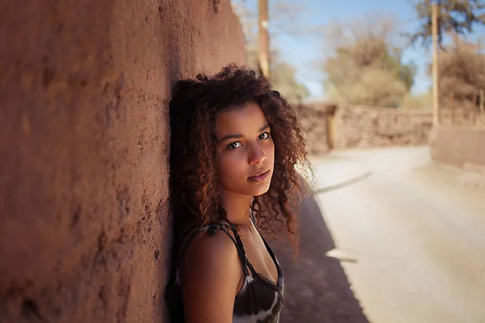 Romanian photographer captures a woman against a rustic wall, showcasing diverse global beauty.