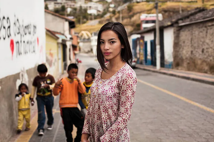 Photograph of a woman from one of 121 countries, showcasing global beauty, standing on a street with children in the background.