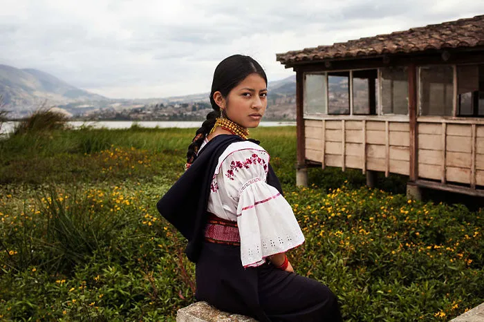 Woman in traditional attire by a rustic building, showcasing diverse beauty in nature for Romanian photographer's project.