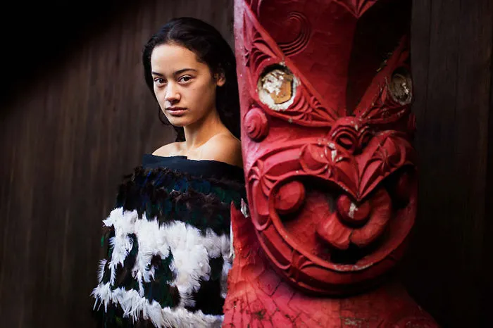Woman in traditional attire beside a red wooden sculpture, captured by Romanian photographer highlighting beauty worldwide.