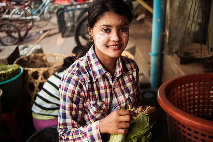Woman from 121 countries project by Romanian photographer, smiling and holding leaves in a market setting.