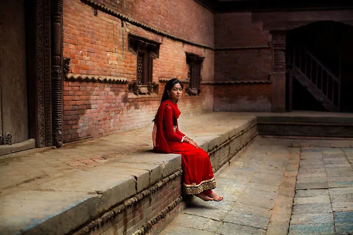 Woman in red dress sitting on ancient brick structure, highlighting diverse beauty captured by Romanian photographer.