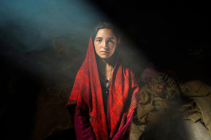 Woman in vibrant red shawl standing in soft light, captured by a Romanian photographer showcasing global beauty.