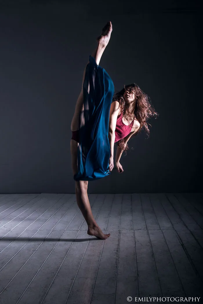 Ballet dancer performing a high kick gracefully in a dimly lit studio.