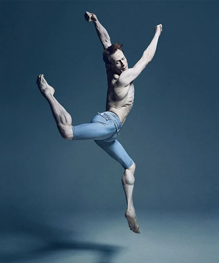Ballet dancer in mid-air leap, wearing blue tights, showcasing the art and cost of applause in ballet.