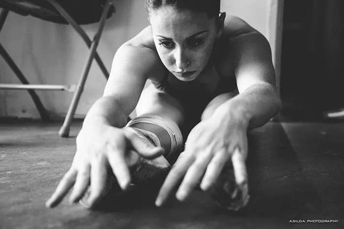 Ballet dancer stretching on the floor, focused and preparing for performance.