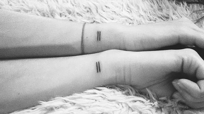 Matching sister tattoos of small black lines on wrists, symbolizing sibling bond.