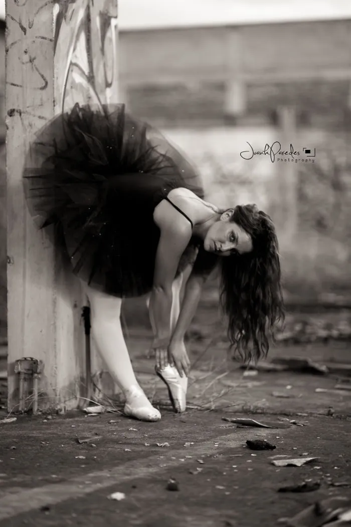 Ballerina in a black tutu adjusting pointe shoes, representing the cost of applause in ballet performance.