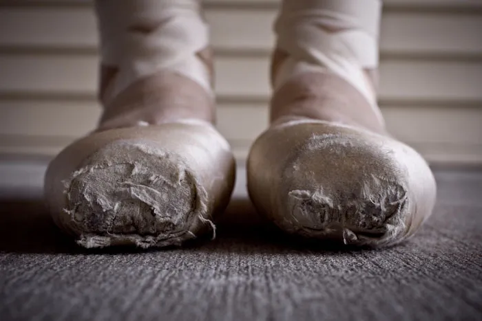 Worn ballet pointe shoes on a dancer's feet, highlighting the cost and dedication of ballet.
