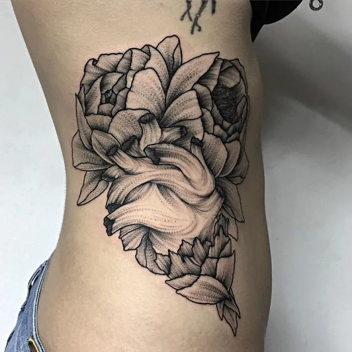 Tattoo of intricate floral design on person's side, created by Russian artist, featuring dark and eerie creature elements.