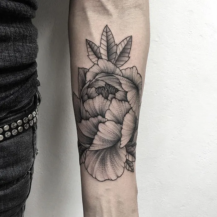 Russian artist's dark tattoo of floral design on forearm, showcasing intricate shading and detail.