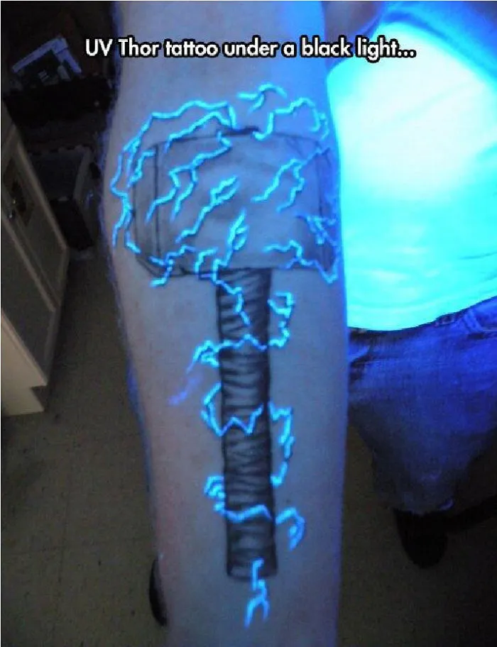 Glow in the dark tattoo of Thor's hammer under black light on an arm.