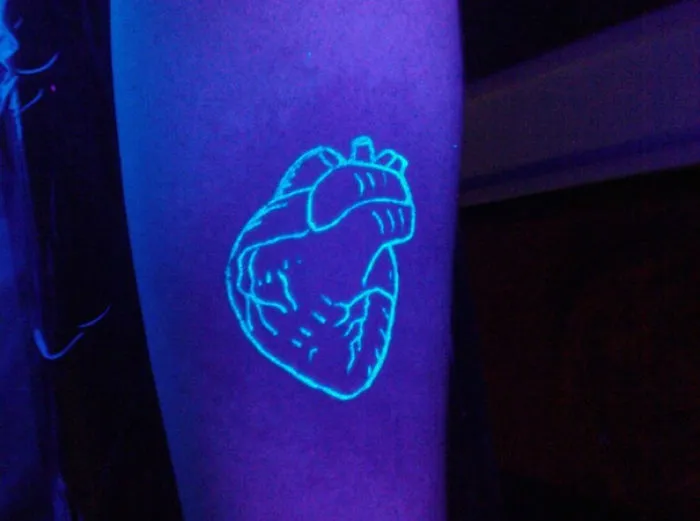 Glow in the dark tattoo of a heart design on an arm, visible under black light.