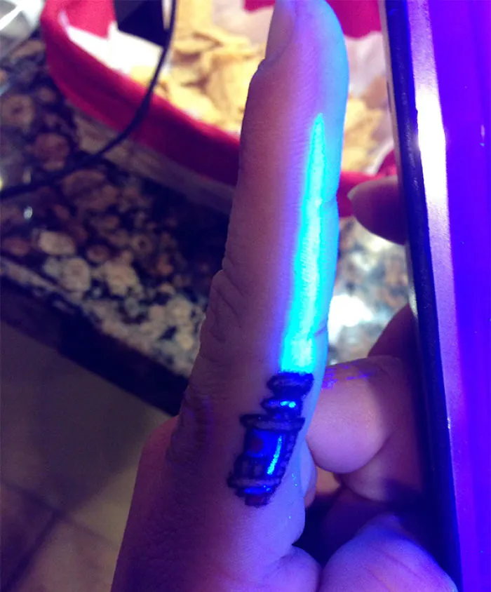 Glow in the dark tattoo on a finger illuminated under black light, revealing vibrant blue and purple hues.