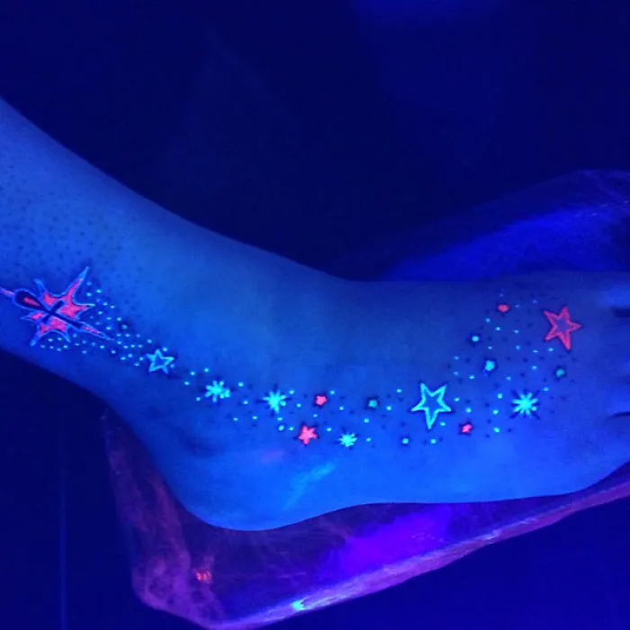 Glowing stars and patterns on a foot tattoo under black light.