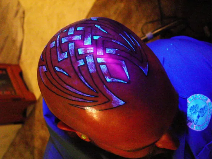 Glow in the dark tattoo design on a shaved head, illuminated under black light.