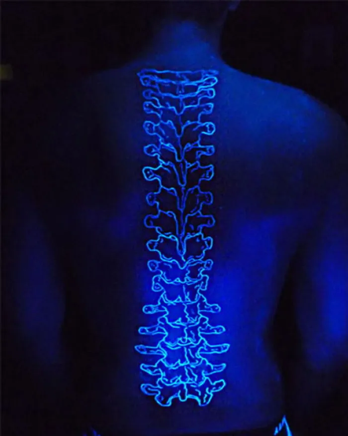 Glow in the dark tattoo of a spine design visible under black light on a person's back.