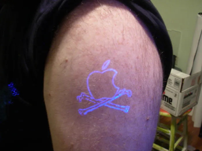 Glow in the dark tattoo of an apple with crossed bones, illuminated under black light.
