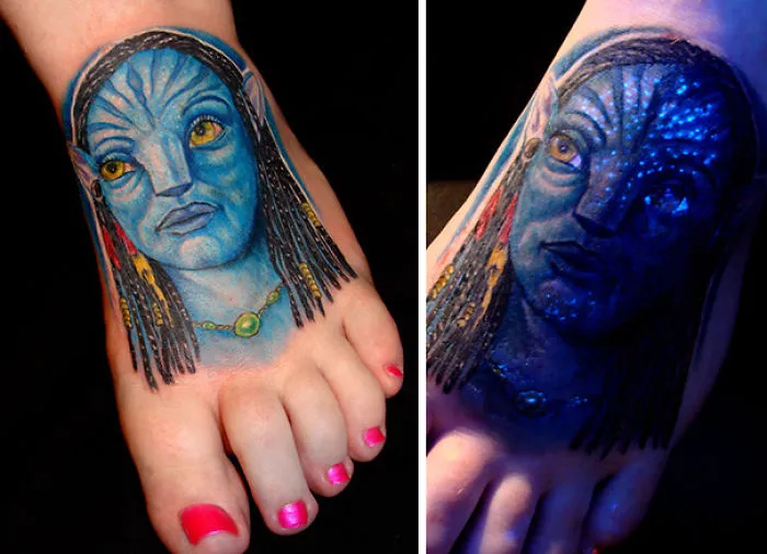 Glow in the dark tattoo of a blue-skinned character on a foot, visible under black light.