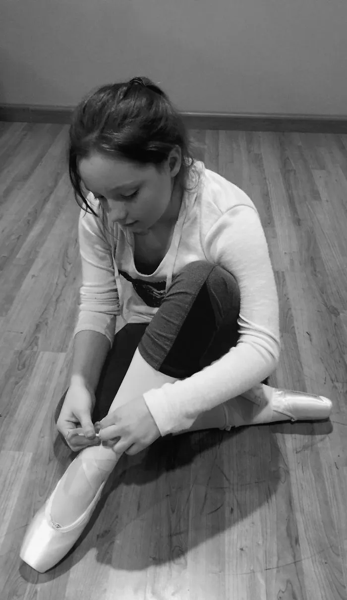 Young dancer tying ballet shoes on wooden floor, celebrating Ballet Day.