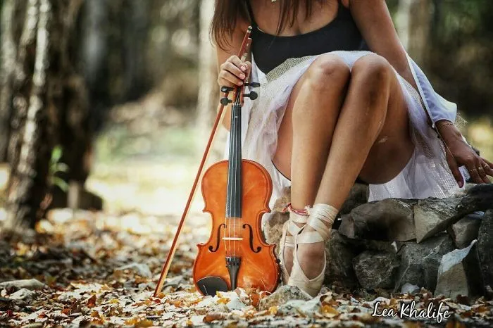 Ballet dancer with a violin outdoors, wearing pointe shoes and a white skirt, celebrating Ballet Day amidst autumn leaves.