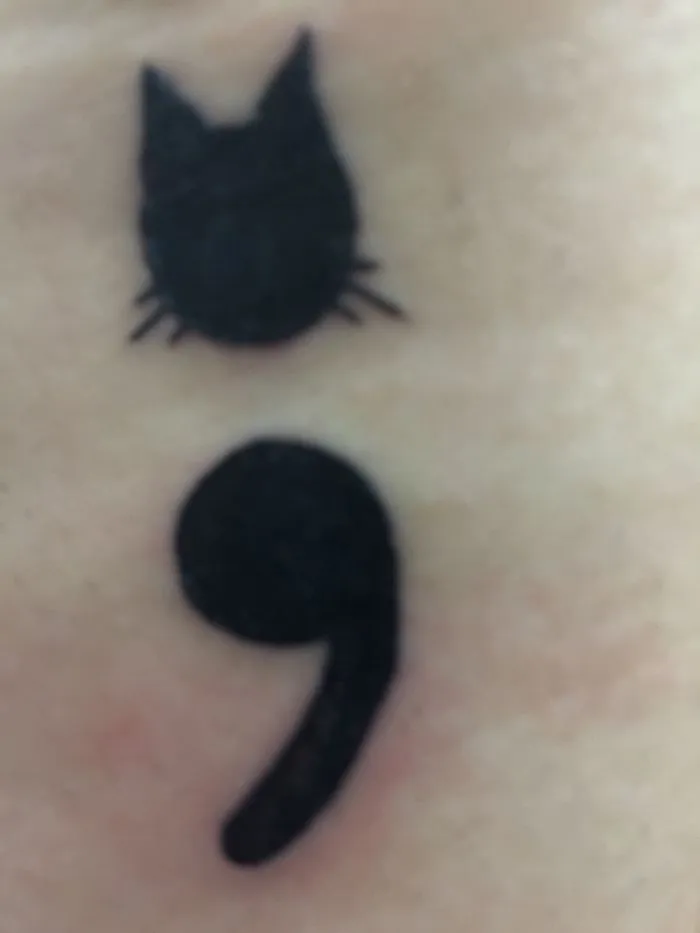 Minimalist tattoo of a cat silhouette above a semicolon on skin.