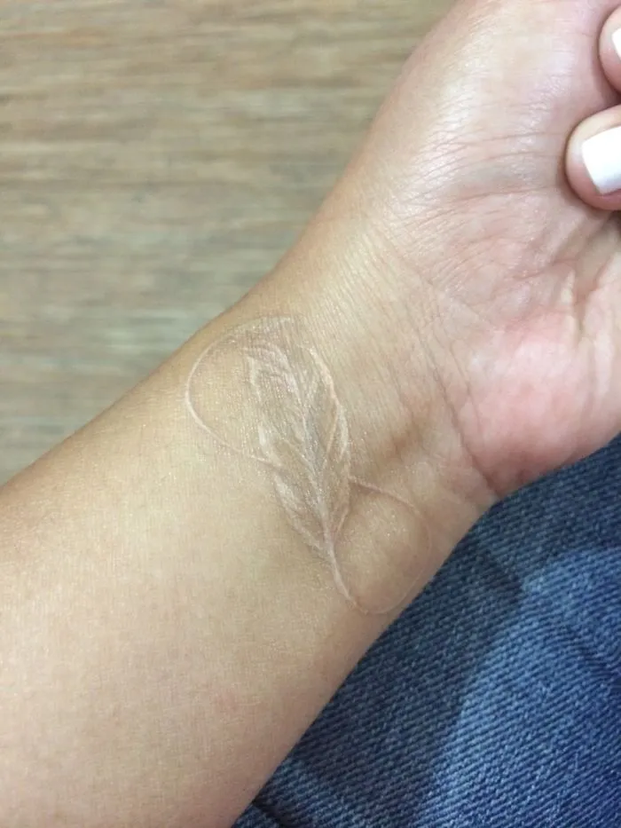Minimalist tattoo of a white ink feather on a wrist.
