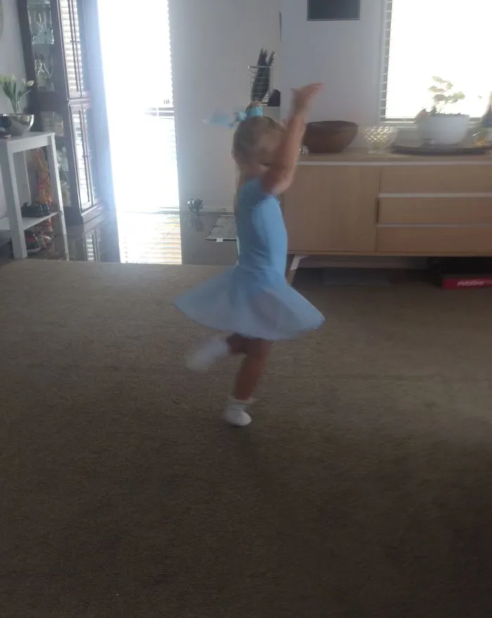 Young girl in a blue ballet dress twirling in a living room, celebrating Ballet Day.