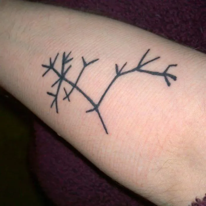 Minimalist tattoo of abstract branches on a person's forearm.