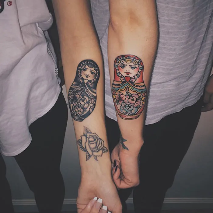 Matching sister tattoos featuring colorful and black-and-white matryoshka dolls on forearms, symbolizing sisterly bond.