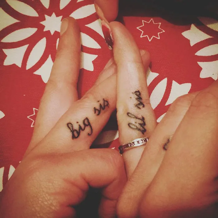 Close-up of fingers with "big sis" and "lil sis" tattoos, symbolizing a sister bond.