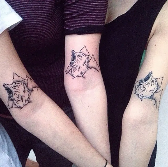 Matching wolf tattoos on sisters' arms symbolizing their strong bond.