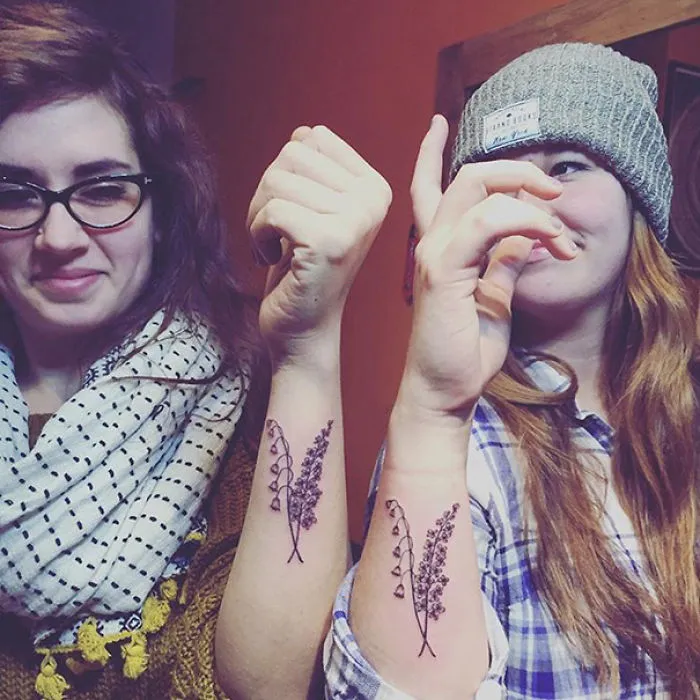 Sisters showing matching floral tattoos on their forearms, symbolizing their bond.