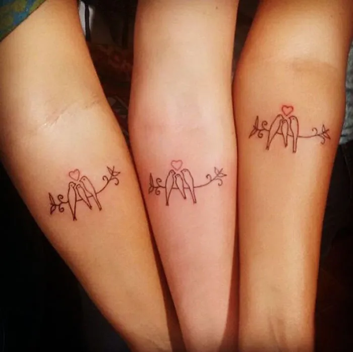 Three forearms with matching sister tattoos of birds on a branch, symbolizing sisterly bond.