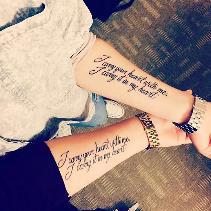 Two matching sister tattoos on forearms read "I carry your heart with me, I carry it in my heart."