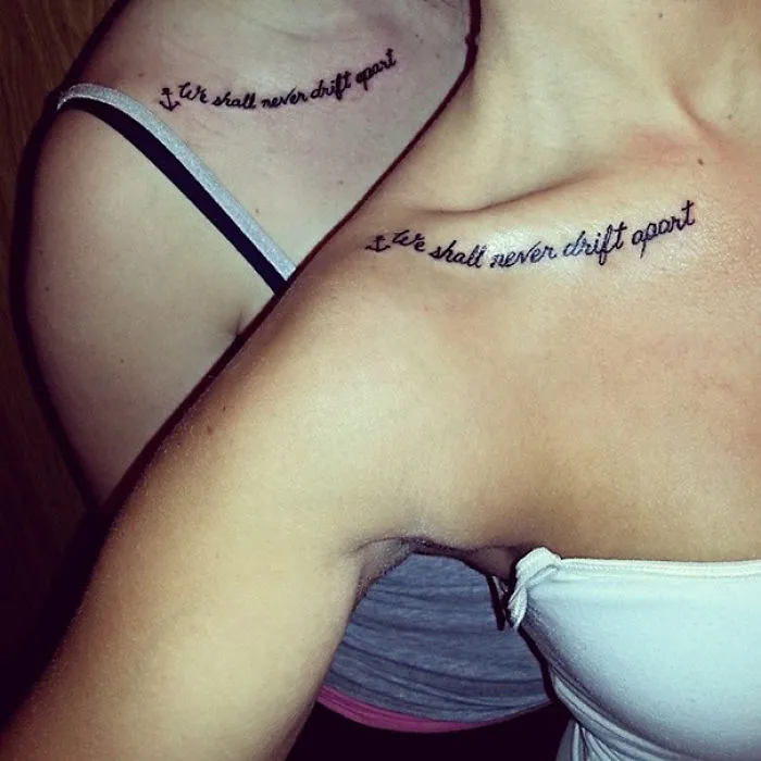Matching sister tattoos on shoulders saying "We shall never drift apart" in cursive font, symbolizing a strong bond.