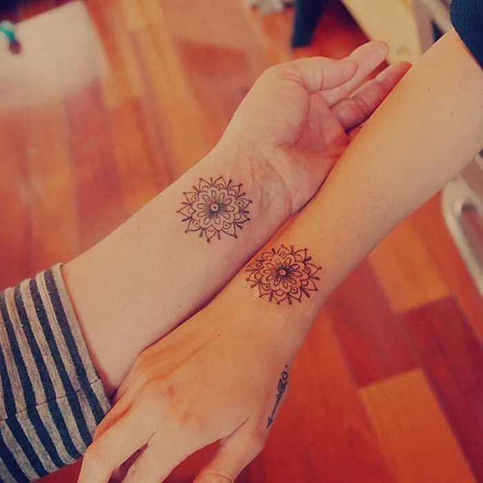 Matching sister tattoos on wrists featuring intricate mandala designs, symbolizing a strong sibling bond.