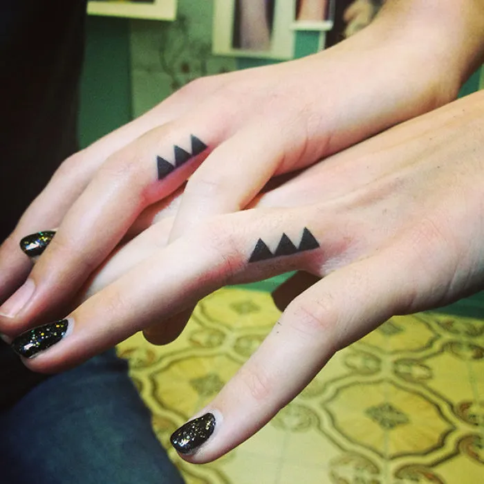 Minimalist sister tattoos on fingers, featuring three black triangles.