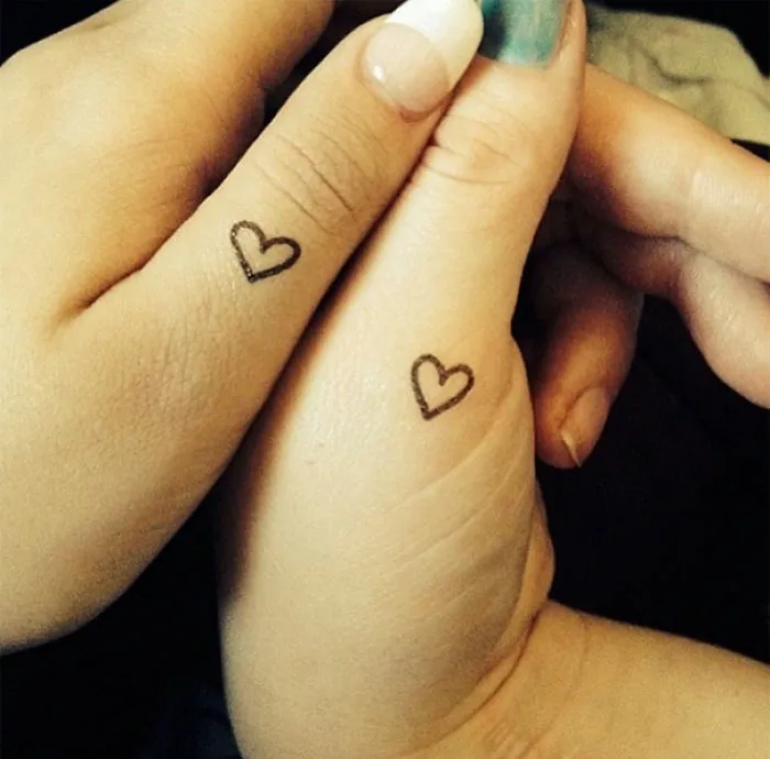Two hands showcasing heart sister tattoos to symbolize a strong bond.