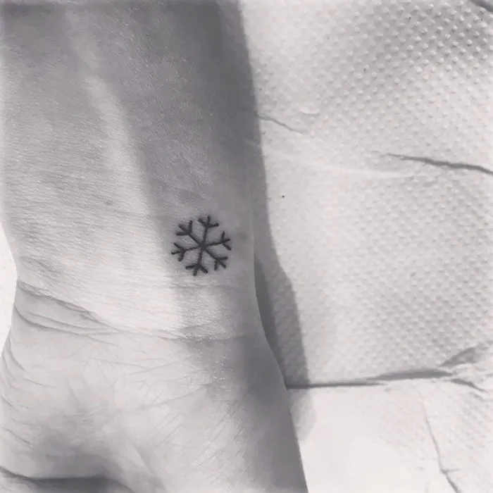 Minimalist snowflake tattoo on a wrist, showcasing simple ink design inspiration.