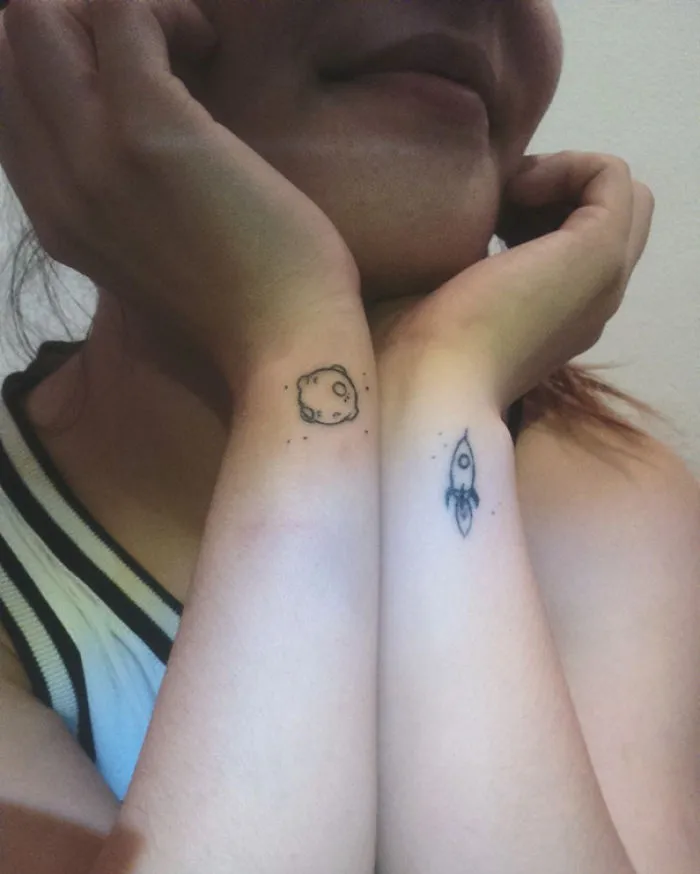 Minimalist tattoos of a planet and rocket on forearms, showcasing simple ink designs.